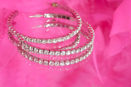 glamorous diamond earrings on vanity mirror with a pink feather boa in the background ( short depth of field)の写真素材