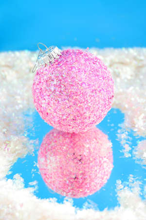 pink sparkly christmas ball with reflection on blue surrounded by fake snowの写真素材