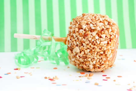 caramel candy apple with peanuts on a stick with green decorative background for a partyの写真素材