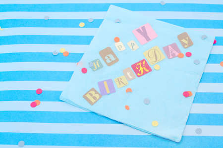 Happy birthday cut out letters on blue napkin with confettiの写真素材