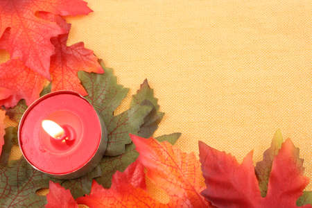 autumn leaf background or border frame  in orange, red, and green with lit tea light candleの写真素材