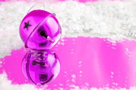 pink christmas bell with reflection on blue surrounded by fake snowの写真素材