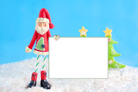 slim santa claus christmas decoration holding a blank white sign for text on fake snow and blue background の写真素材