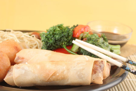 delicious chinese lo mein noodles and stir fry vegetables with cashews with chicken balls, spring rolls, soya  sauce and chopsticks on a bamboo placematの写真素材