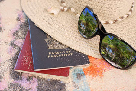 travel passports on beach towel and sand with hat and sunglasses showing a reflection of beautiful tropical palm trees の写真素材