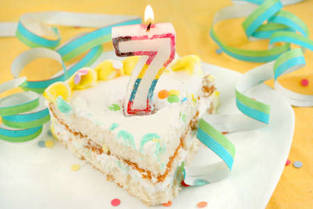 slice of seventh birthday cake with lit candle, confetti, and ribbon (shallow depth of field)の写真素材