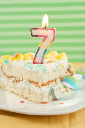 slice of seventh birthday cake with lit candle, confetti, and ribbon (shallow depth of field)の写真素材