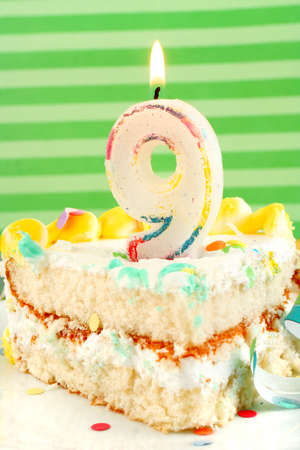 slice of nineth birthday cake with lit candle, confetti, and ribbon (shallow depth of field)の写真素材