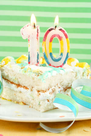slice of tenth birthday cake with lit candle, confetti, and ribbon (shallow depth of field)の写真素材