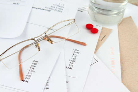 Different bills to be paid. envelopes and eyeglasses with red pills, and water to soothe the headache of paying billsの写真素材
