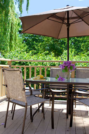 Wooden backyard deck with outdoor table, chairs and shade umbrella, lemons and clematis arrangementの写真素材