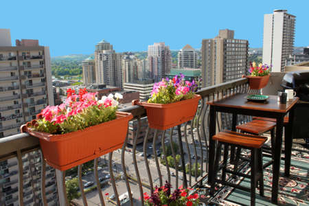 Rooftop patio with table and stool chairs, colorful flower baskets along a balcony railing with Calgary building skyline in the backgroundの写真素材