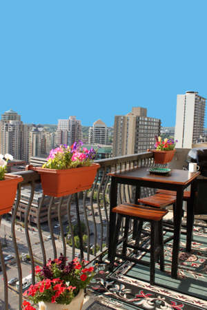 Rooftop patio with table and stool chairs, colorful flower baskets along a balcony railing with Calgary building skyline in the backgroundの写真素材