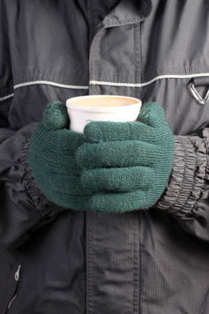 Person with green mittens, scarf and winter coat holding a warm beverage in a white cup on a cold  dayの写真素材