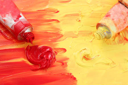 Red and yellow colors of artist's oil paints spilling out into a smudged painted backgroundの写真素材
