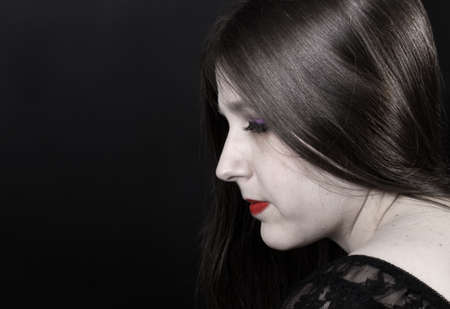Woman with porcelain white skin, red lipstick and long brown shiny hair on a black backgroundの写真素材