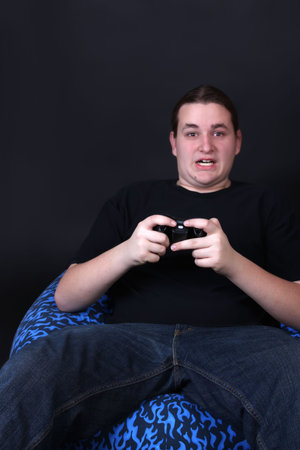 Teenager holding a video game controller with intense surprised expression on his face while sitting...