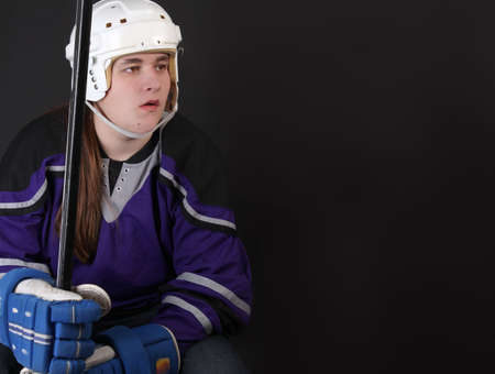 Teen male hockey player with helmet, gloves, and stick on a dark grey backgroundの写真素材