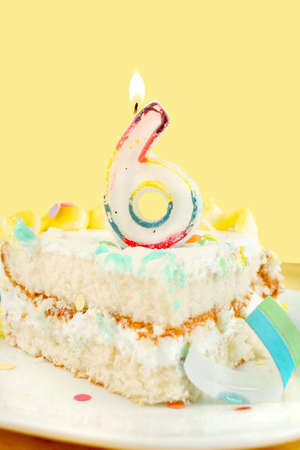 slice of sixth birthday cake with lit candle, confetti, and ribbon (shallow depth of field)の写真素材