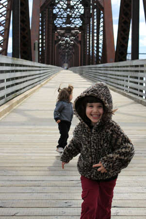 Two cute little girls running towards the camera laughing and playing on a wooden bridgeの写真素材