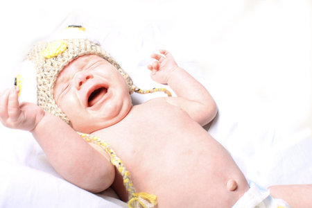 Little month old baby crying wearing hat and showing belly button on a white background