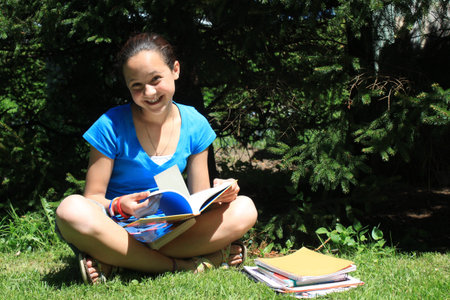 Pretty young girl reading a book sitting in the sunshine outdoors