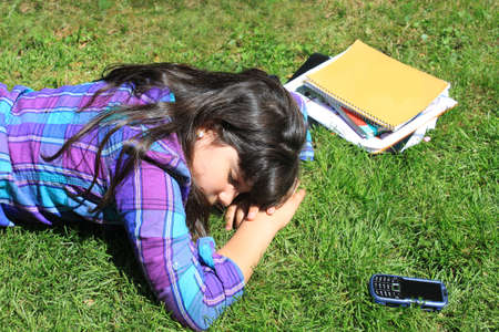 A young girl takes a nap or break from her school studies, laying on the grass outdoorsの写真素材