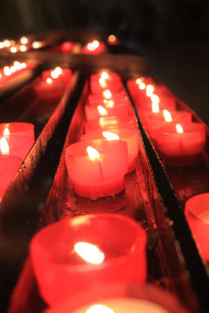 Lit candles in small red holders in a row, each one lit for a prayer in a churchの写真素材