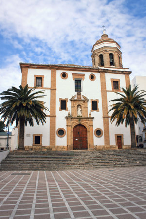 Church in the centre of Ronda Spain, with courtyard with palm trees and cloudy blue skyの写真素材