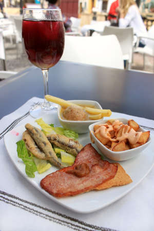 Hot tapas consisting of fried sardines, bacon on a tostada, fries with sauce and meatball, with a glass of sangria, food from Andalusia, Spainの写真素材