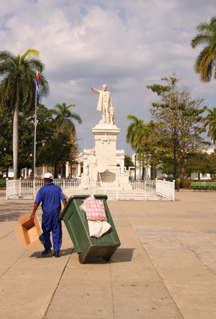 CIENFUEGOS, CUBA - FEBRUARY 25, 2014: A garbage man drags green bin through Plaza Jose Marti in Cienfuegos, Cuba on February 25, 2014のeditorial素材