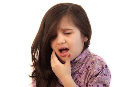 Cute little girl with her hand held to her face with painful expression showing toothacheの写真素材