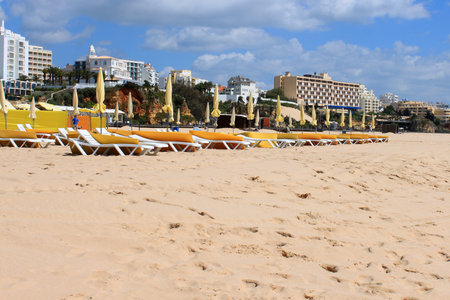 Loungers and parasols for shade along the golden sandy shored beach of Praia da Rocha with resort buildings in the background in Algarve, Portugalの写真素材
