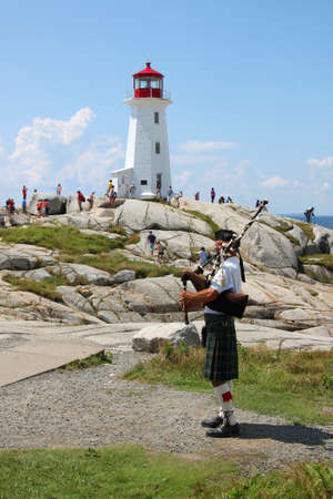 August 6, 2014, Peggy's Cove, Nova Scotia: Bagpiper playing music in front of the lighthouse in touristic Peggy's Cove, Nova Scotia, Canada のeditorial素材