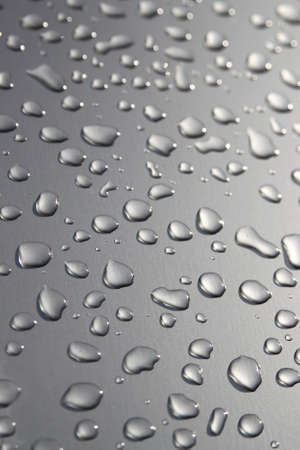 Raindrops on a silver surface with sun shining adding a light effectの写真素材