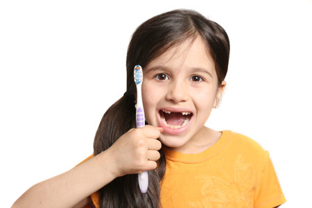 Little seven year old girl shows big smile showing missing top front teeth and holding a toothbrush...