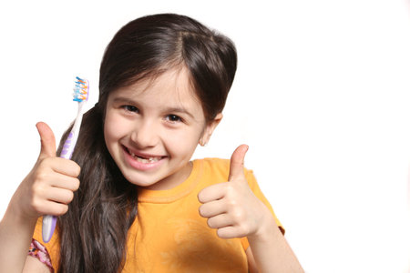 Little seven year old girl shows big smile showing missing top front teeth and holding a toothbrush...