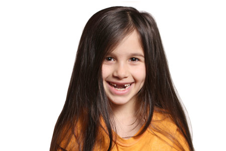 Little seven year old, happy girl shows big smile showing missing top front teeth on a white...