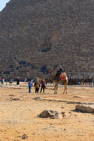 GIZA PLATEAU, EGYPT - JAN. 31, 2016: Tourists and visitors at the bottom of the Grand Pyramid walking, going on camel and horseback in the golden desert sands in Egyptのeditorial素材
