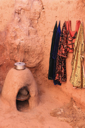 Traditional Moroccan stove made out of sandstone with a pot cooking food and robes hanging on wall