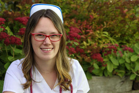 Young smiling female nurse portrait wearing white scrubs, cap and a stethoscope around her neck  outdoors during the Fallの写真素材