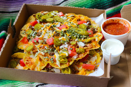 Take out box with nachos topped with beef, jalapenos,tomatoes, onions and cheese, with salsa and sour cream on the side for dippingの写真素材