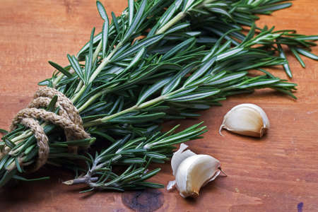 Bunch of fresh rosemary and  garlic  on old wooden backgroundの写真素材