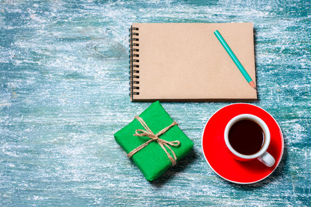 Notepad, cup of coffee, box with gift on a blue wooden table. Space for text, top viewの写真素材