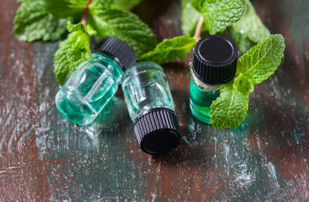 Essential oil of peppermint in small bottles, fresh green mint on wooden background, selective focusの写真素材