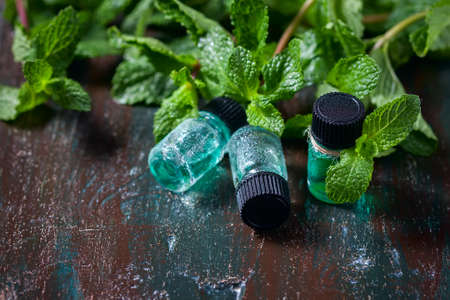 Essential oil of peppermint in small bottles, fresh green mint on wooden background, selective focusの写真素材