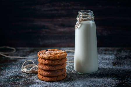 Oatmeal cookies with raisins, chocolate and milk in bottles, wood background, selective focusの写真素材