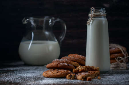 Oatmeal cookies with raisins, chocolate and milk in bottles, wood background, selective focusの写真素材