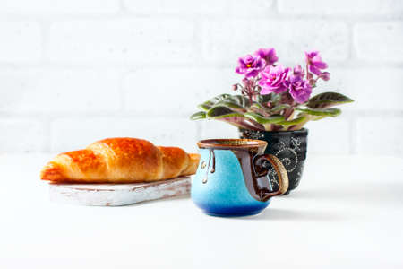 Cup of black coffee with croissant and African Violet on white table. Selective focusの写真素材