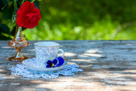 Porcelain cup of tea and beautiful spring flowers in vase on a wooden table in the garden. Summer party. Selective focusの写真素材